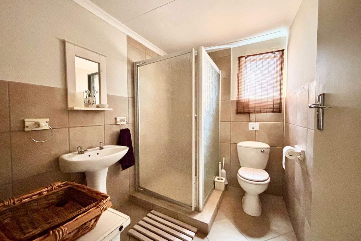 A functional bathroom featuring a pedestal sink, a glass-enclosed shower, and a toilet, finished with neutral wall and floor tiling.