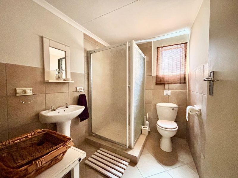 A functional bathroom featuring a pedestal sink, a glass-enclosed shower, and a toilet, finished with neutral wall and floor tiling.