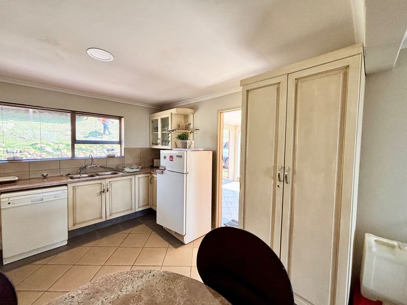 A functional kitchen featuring tiled flooring, ample built-in cabinetry, a double basin sink, and a large built-in pantry cupboard.