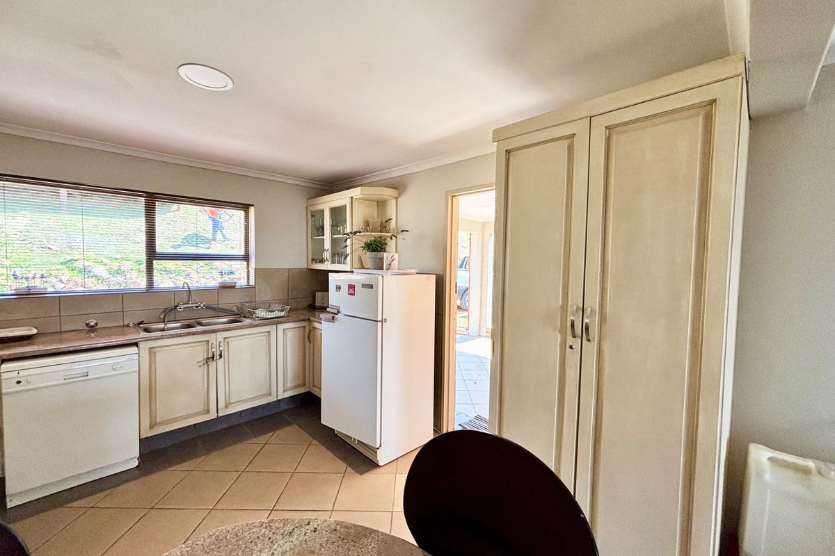 A functional kitchen featuring tiled flooring, ample built-in cabinetry, a double basin sink, and a large built-in pantry cupboard.