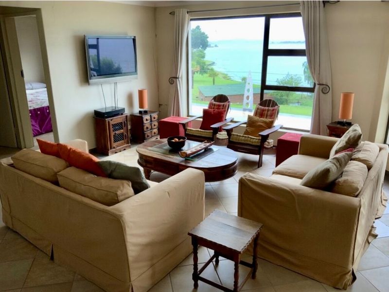 A comfortable living room featuring large windows with scenic water views and tiled flooring, offering a bright and inviting space.