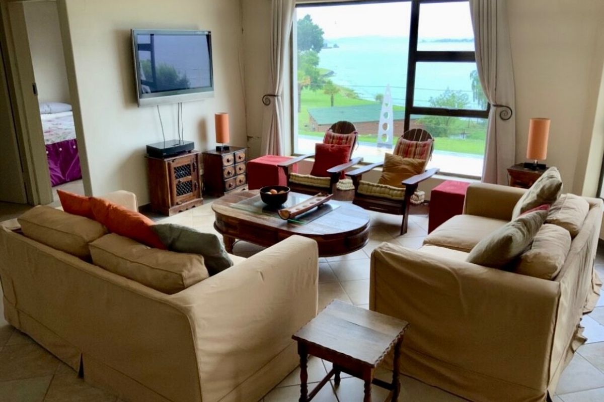 A comfortable living room featuring large windows with scenic water views and tiled flooring, offering a bright and inviting space.