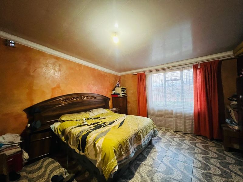 A bedroom featuring tiled flooring, a security gate on the window, and decorative wall finishes, offering a functional space with potential for modernization.