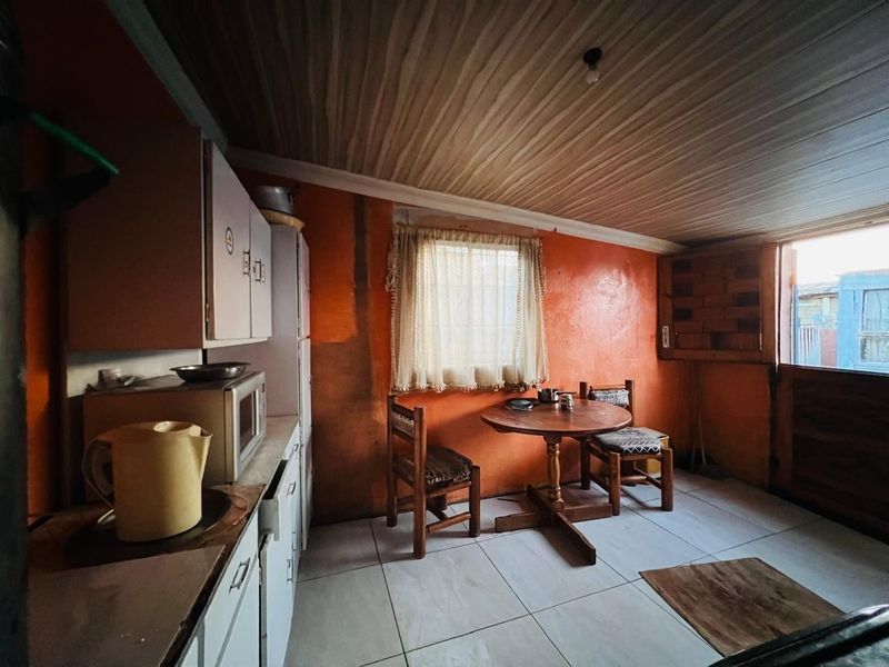 A compact kitchen featuring tiled flooring, timber ceiling, and built-in cabinetry, offering a functional space with potential for cosmetic updates.