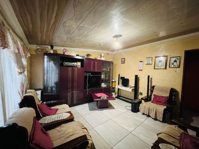 A living room featuring tiled flooring, a textured ceiling, and a large built-in wall unit, offering potential for cosmetic updates and modernization.