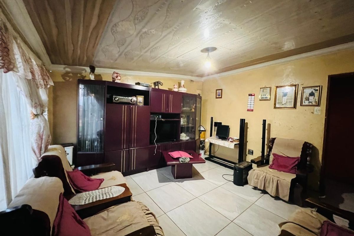 A living room featuring tiled flooring, a textured ceiling, and a large built-in wall unit, offering potential for cosmetic updates and modernization.