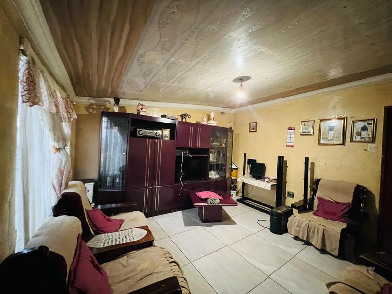 A living room featuring tiled flooring and a textured ceiling, currently showing signs of wear and dated wall finishes.