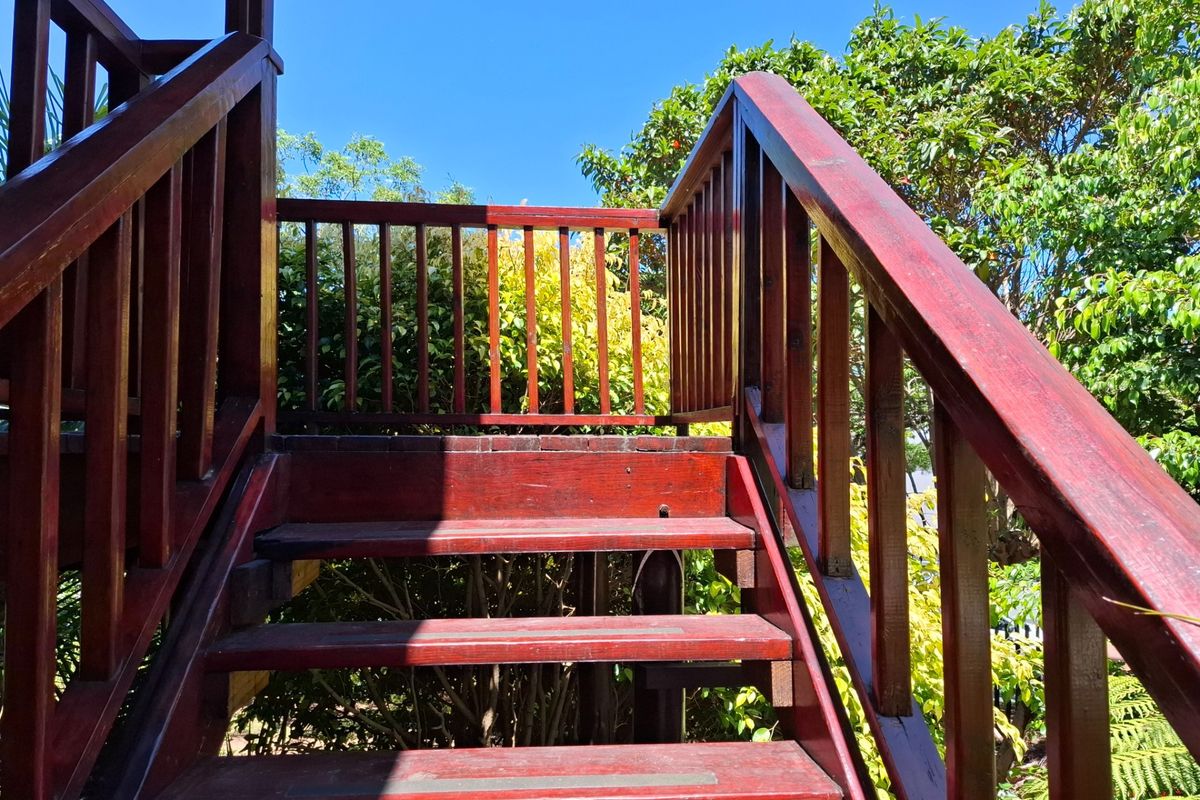 An outdoor timber staircase with balustrades leading to an elevated area, surrounded by established garden greenery.