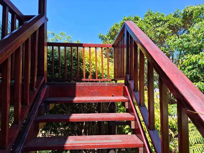 An outdoor timber staircase with balustrades leading to an elevated area, surrounded by established garden greenery.