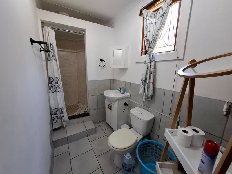 A functional bathroom featuring a shower cubicle, vanity basin, and toilet with neutral wall and floor tiling.