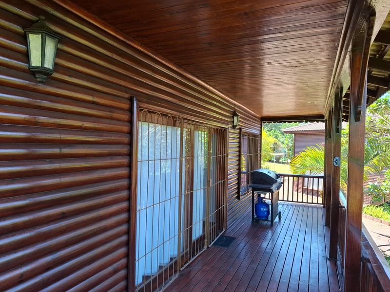 A covered timber balcony featuring wood-paneled walls and ceiling, secure metal gates, and a timber balustrade overlooking the garden area.