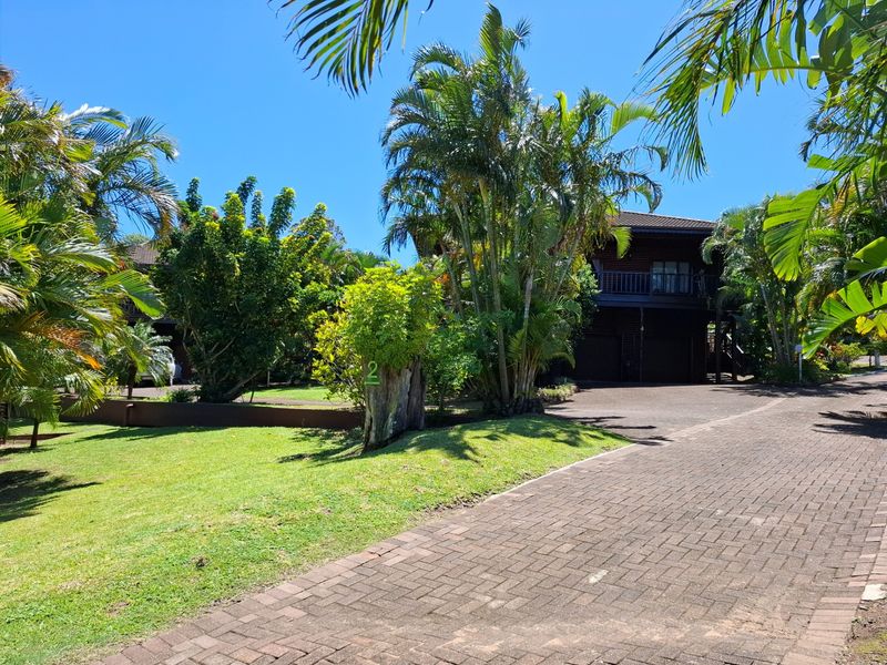 Front view of a multi-story apartment building featuring timber cladding, a paved driveway, and established tropical landscaping.