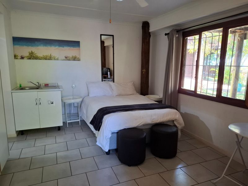 A bedroom featuring tiled flooring, a built-in kitchenette cabinet with a sink, and a window with security bars.