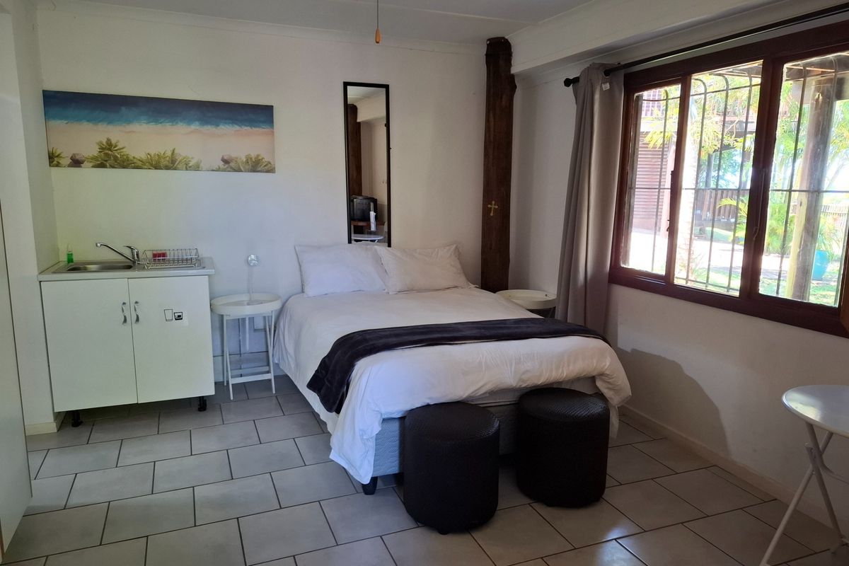 A bedroom featuring tiled flooring, a built-in kitchenette cabinet with a sink, and a window with security bars.