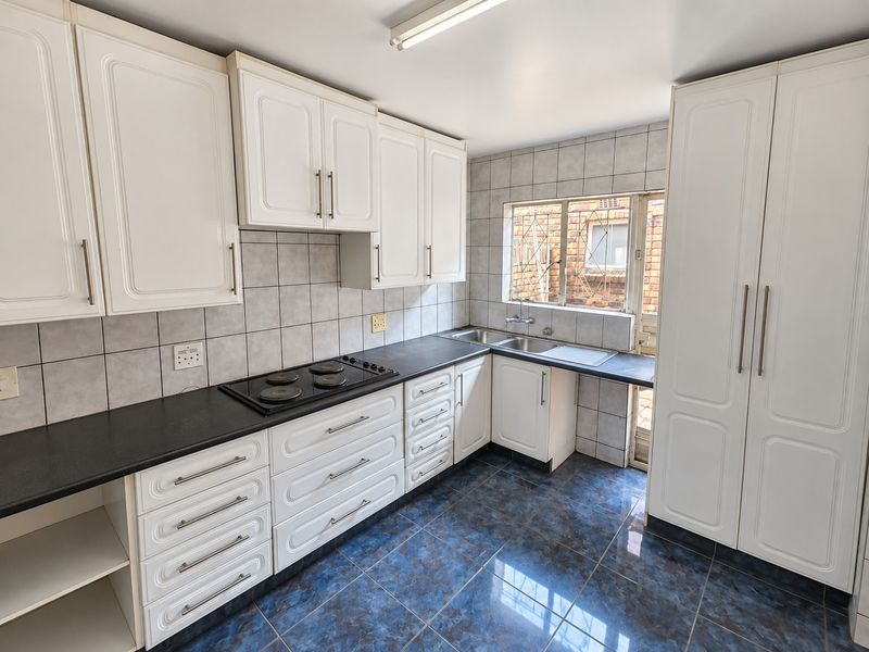 A functional kitchen featuring white built-in cabinetry, a black countertop with an integrated electric hob, double sink, and blue tiled flooring.