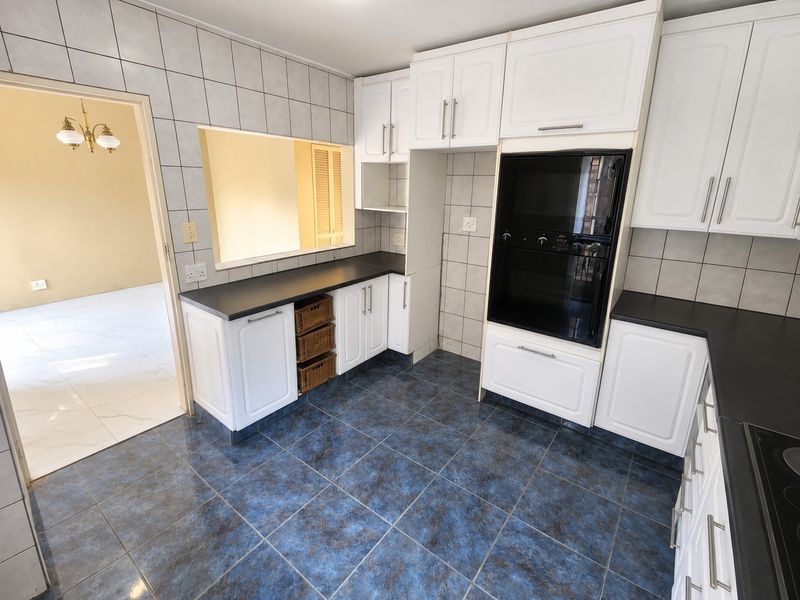 A functional kitchen featuring white cabinetry, dark countertops, built-in oven, and blue ceramic floor tiles with a convenient pass-through window to the adjacent room.