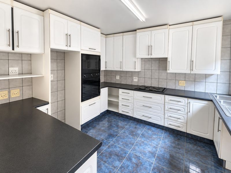 A clean, functional kitchen featuring white cabinetry, dark laminate countertops, built-in oven, electric hob, and blue ceramic floor tiles.