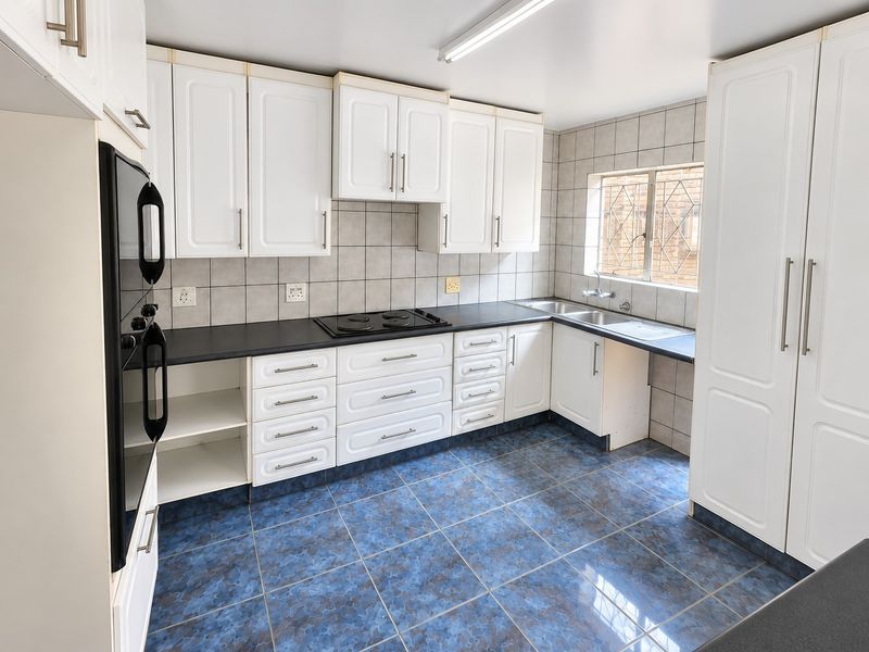 A functional kitchen featuring white built-in cabinetry, dark laminate countertops, an electric hob, built-in oven, and blue tiled flooring.