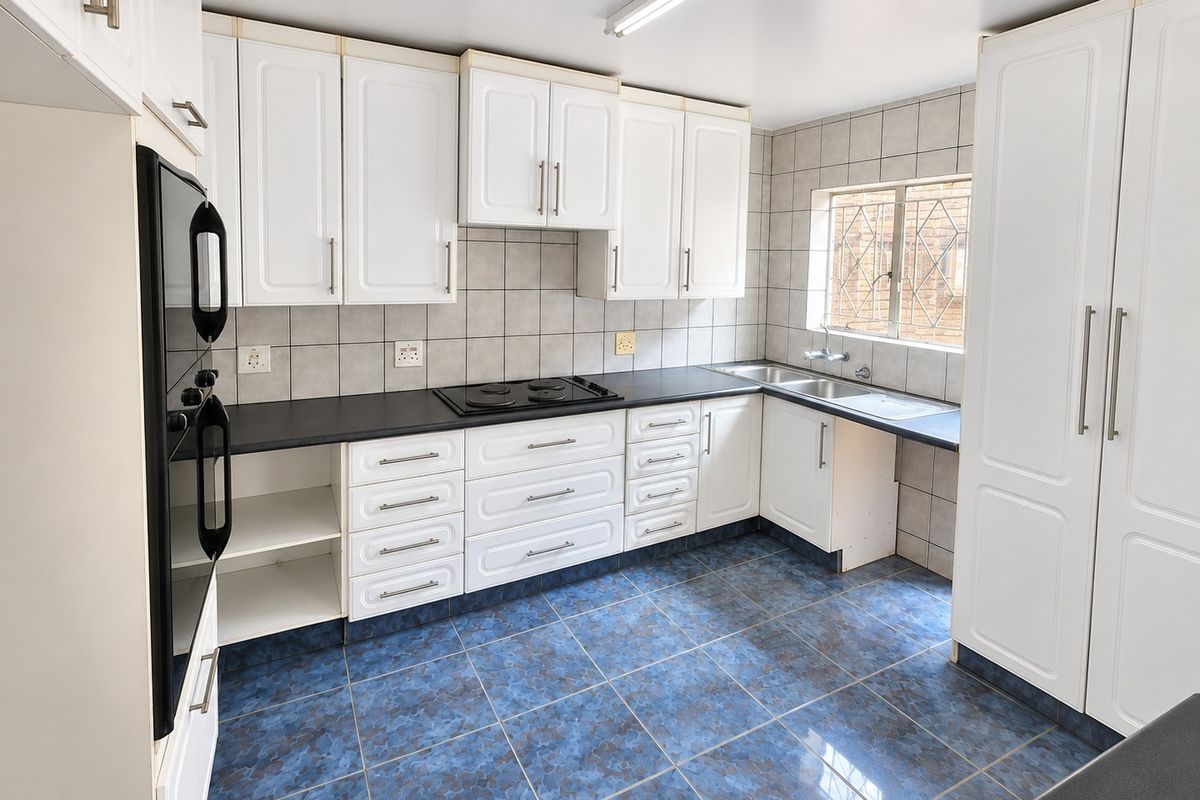 A functional kitchen featuring white built-in cabinetry, dark laminate countertops, an electric hob, built-in oven, and blue tiled flooring.