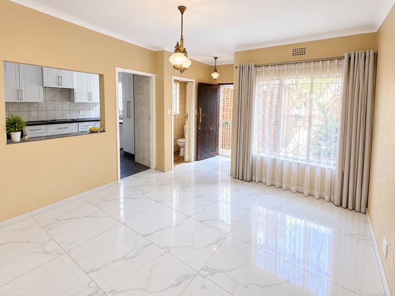 Bright and spacious living area featuring polished marble-look floor tiles, coved cornices, and a convenient pass-through window connecting to the kitchen.