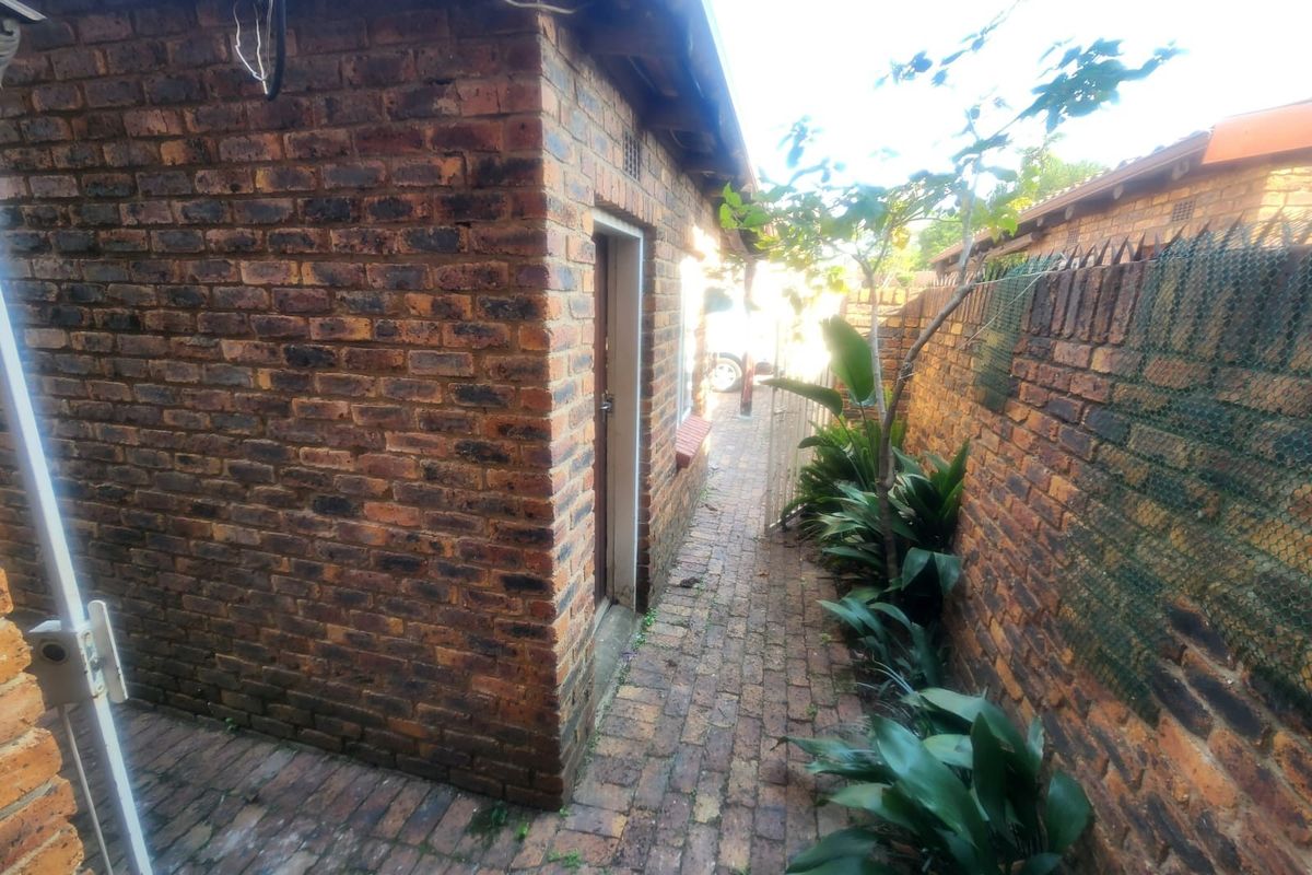 A narrow exterior side passage featuring face brick walls and brick paving, leading towards the rear of the property.