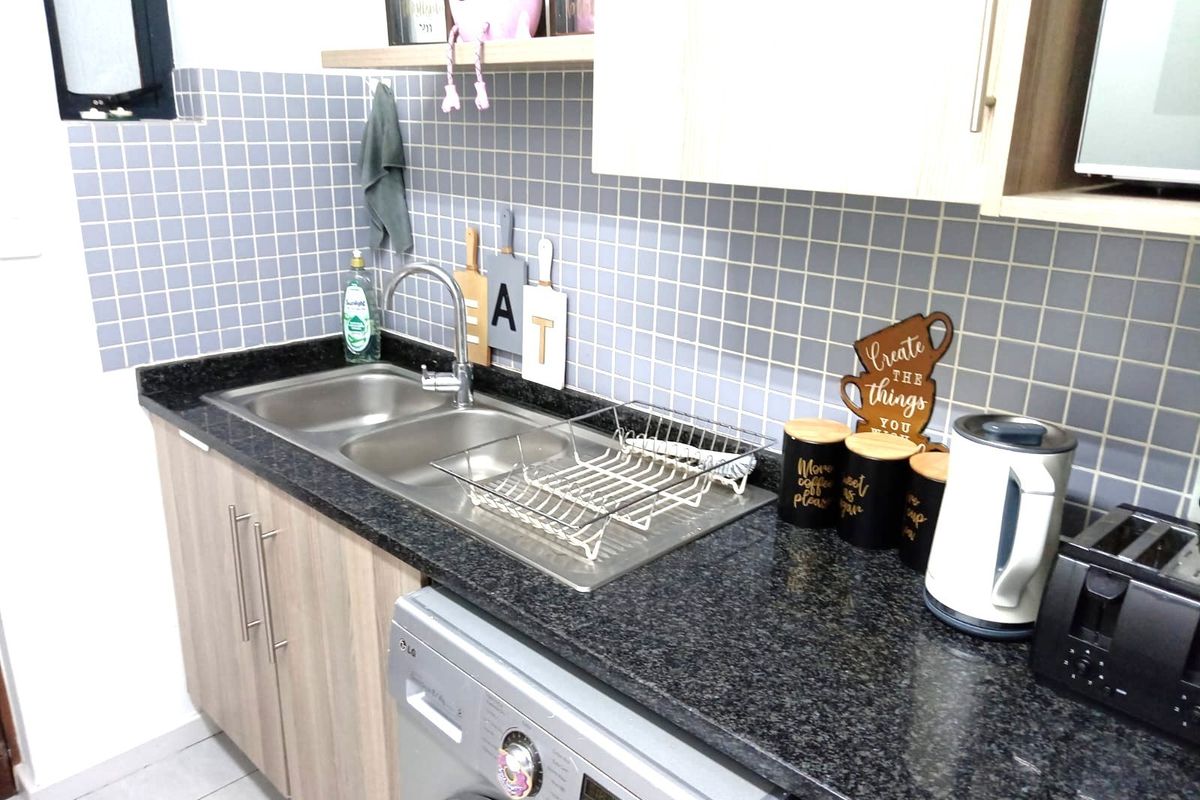 A functional kitchen area featuring granite countertops, a stainless steel double sink, tiled backsplash, and integrated under-counter laundry space.