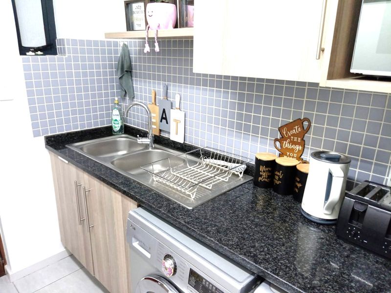 A functional kitchen area featuring granite countertops, a stainless steel double sink, tiled backsplash, and integrated under-counter laundry space.