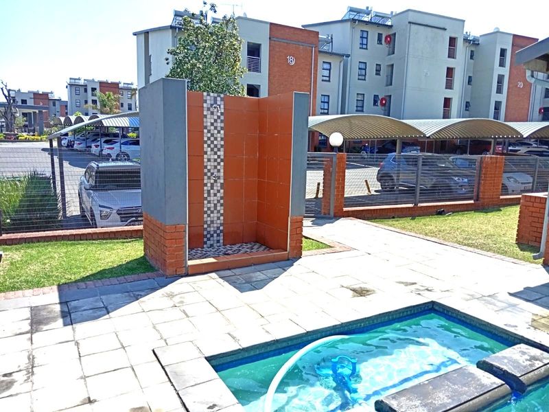 Outdoor pool area featuring a tiled shower, paved deck, and brick boundary wall within a residential apartment complex.