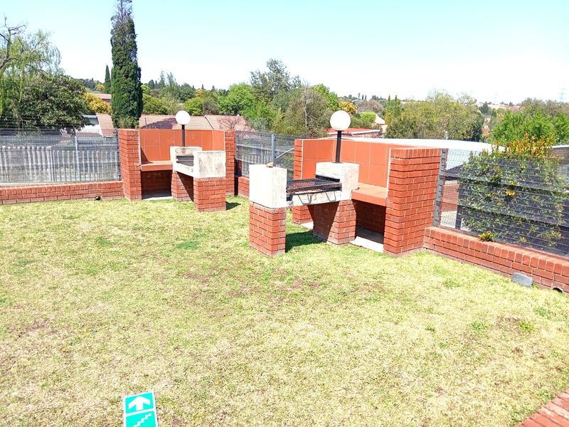 Communal garden area featuring two built-in brick braai stations with integrated lighting, enclosed by brick walls and mesh fencing.