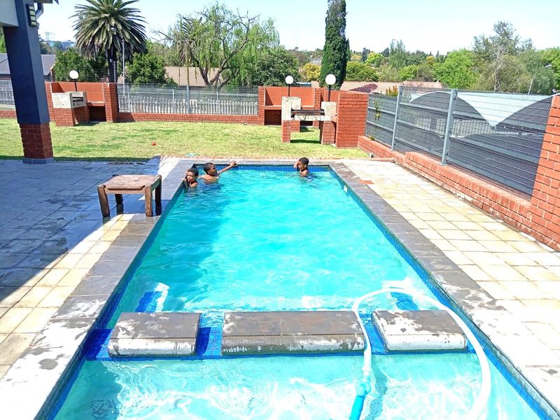 Outdoor pool area featuring a swimming pool, paved surround, and built-in brick braai facilities within a fenced garden setting.