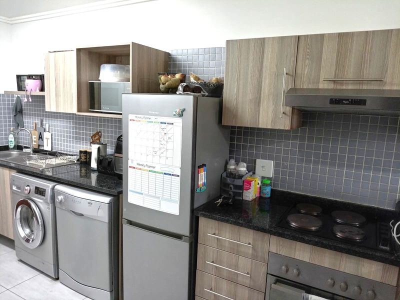 A functional kitchen featuring wood-finish cabinetry, granite countertops, mosaic tile backsplash, and integrated appliances including an oven, hob, and extractor fan.