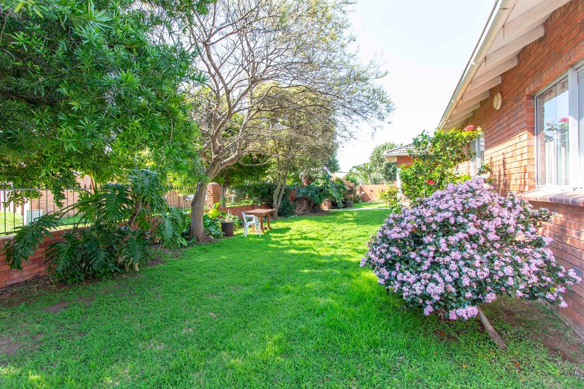 A well-maintained rear garden featuring a lush green lawn, mature trees, and a brick exterior wall of the house.