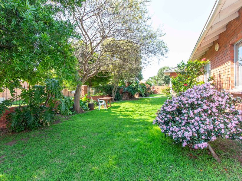 A well-maintained rear garden featuring a lush green lawn, mature trees, and a brick exterior wall of the house.