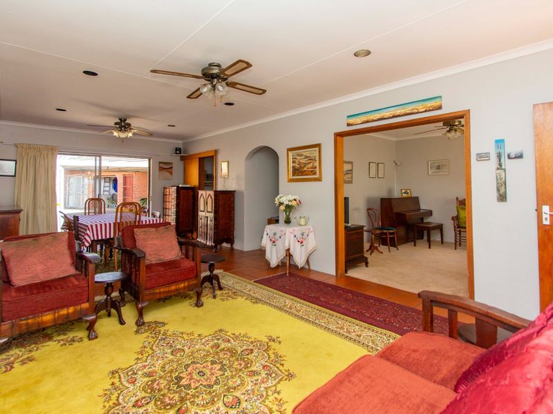 Spacious living area featuring tiled flooring, ceiling fans, and an open archway leading to an adjacent room with carpeted flooring.