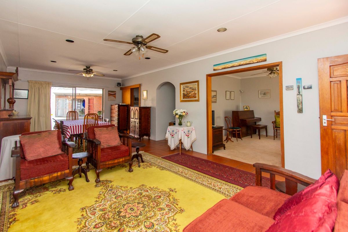 Spacious living area featuring tiled flooring, ceiling fans, and an open archway leading to an adjacent room with carpeted flooring.