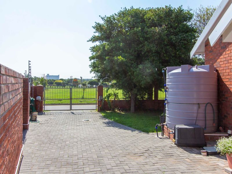 Rear exterior area featuring a paved driveway, brick boundary walls, metal gate, and a large water storage tank.
