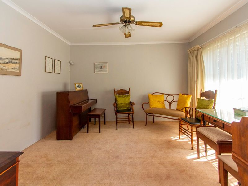 A living room featuring neutral wall finishes, carpeted flooring, a ceiling fan, and a large window allowing for natural light.