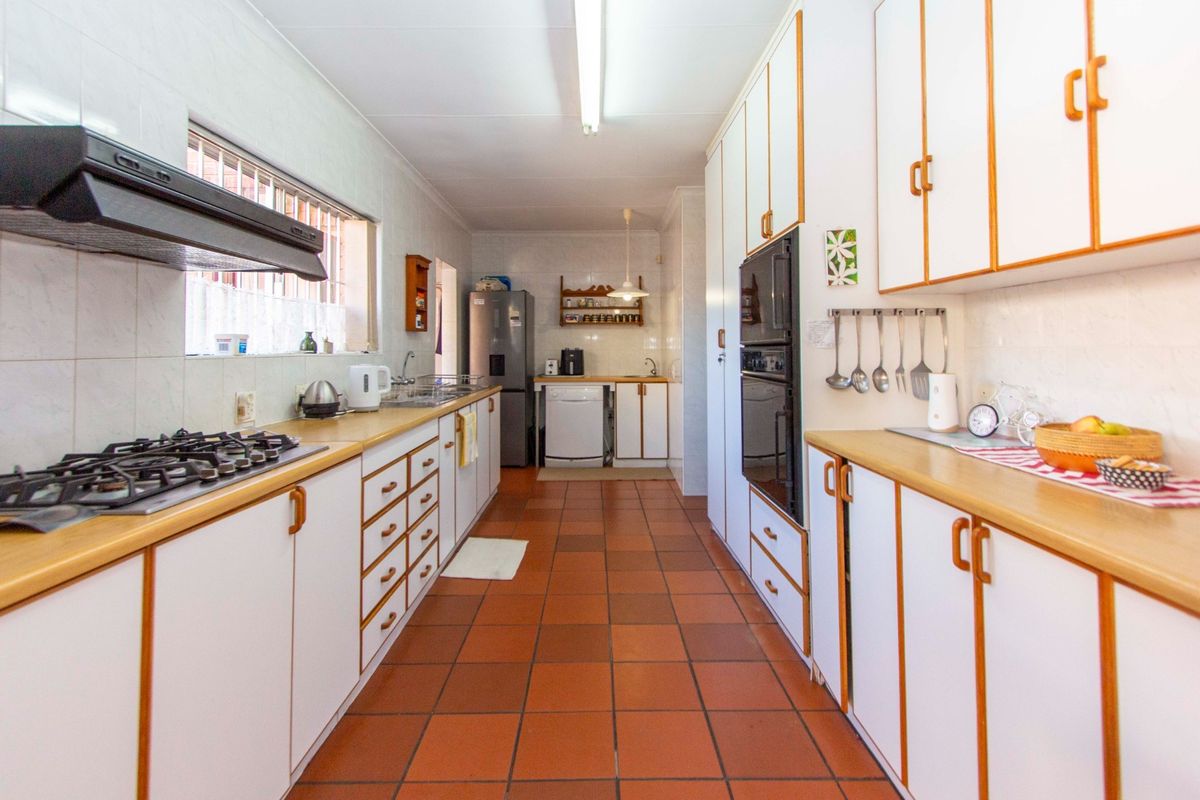 A functional galley-style kitchen featuring white cabinetry with wood trim, gas hob, built-in oven, tiled splashbacks, and durable terracotta-style floor tiles.
