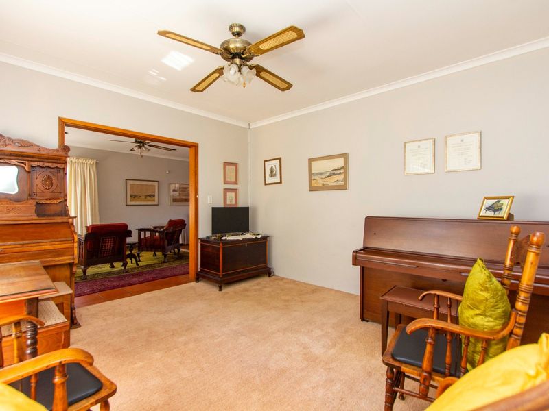 A living room featuring neutral walls, carpeted flooring, and a ceiling fan, with an open doorway leading to an adjacent living space.
