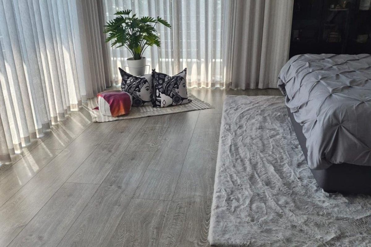 A modern bedroom featuring light-toned laminate flooring, floor-to-ceiling curtains, and a built-in wardrobe, creating a bright and contemporary living space.