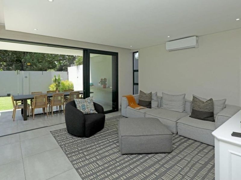 Modern open-plan living area featuring large format floor tiles, recessed lighting, and seamless flow to a covered patio through expansive sliding glass doors.