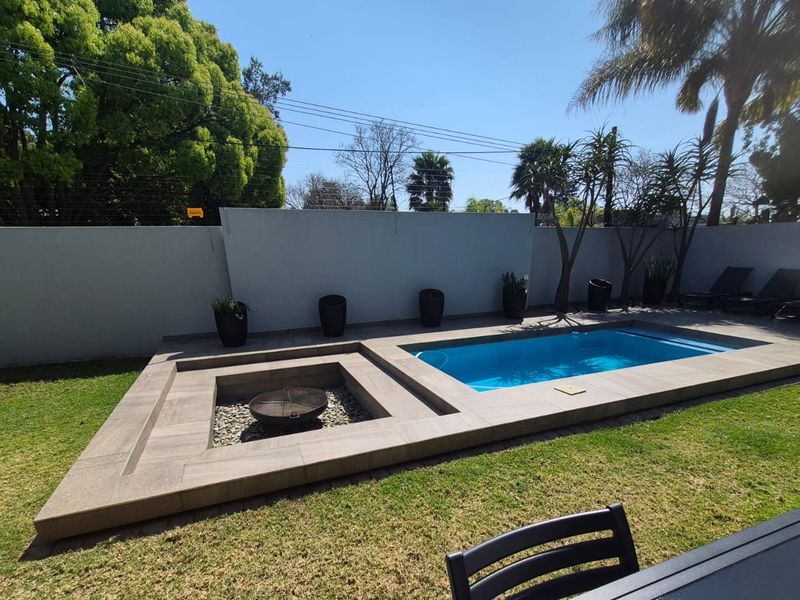 Outdoor entertainment area featuring a swimming pool and a sunken fire pit set within a tiled deck, surrounded by a private garden.