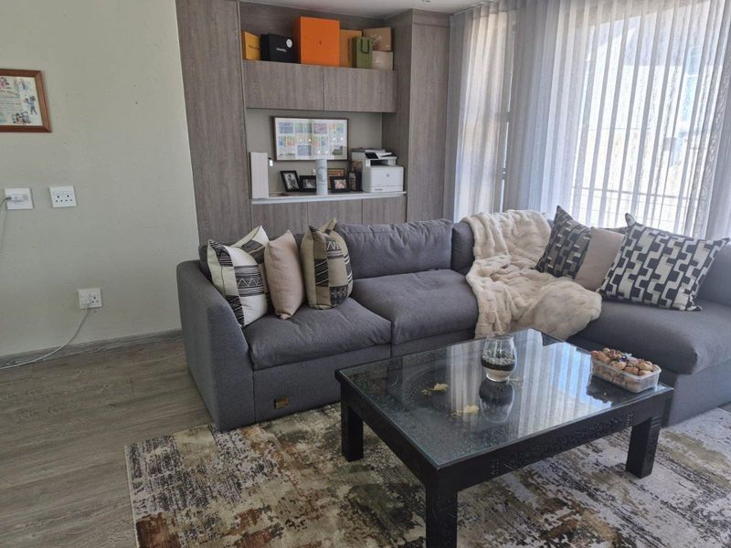 A comfortable living room featuring modern laminate flooring, a custom built-in shelving unit, and floor-to-ceiling sheer curtains allowing for natural light.