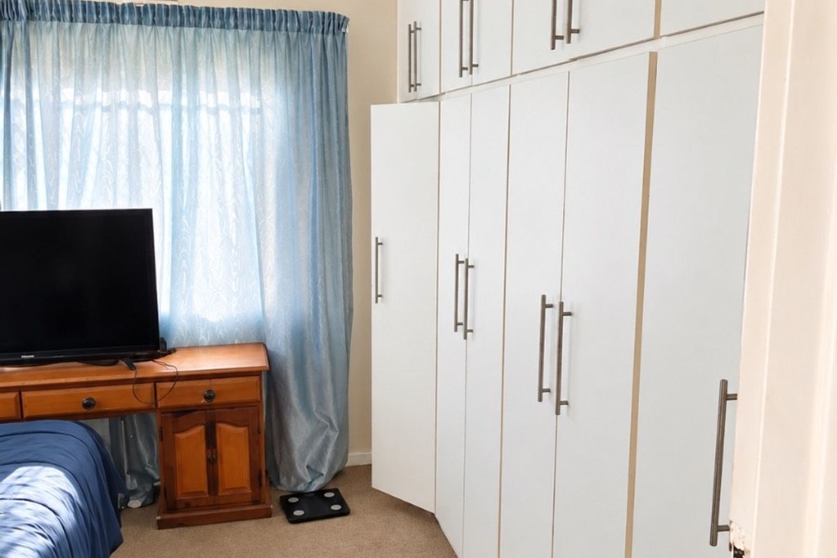A bedroom featuring extensive floor-to-ceiling built-in cupboards and a ceiling fan, providing ample storage space.
