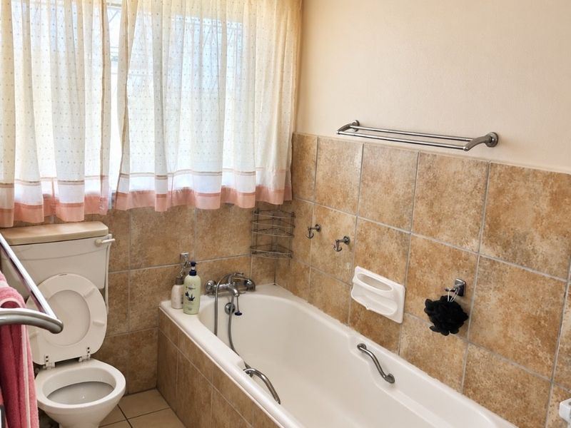A functional bathroom featuring a bathtub, toilet, and neutral-toned wall and floor tiling, offering a classic layout ready for modern updates.