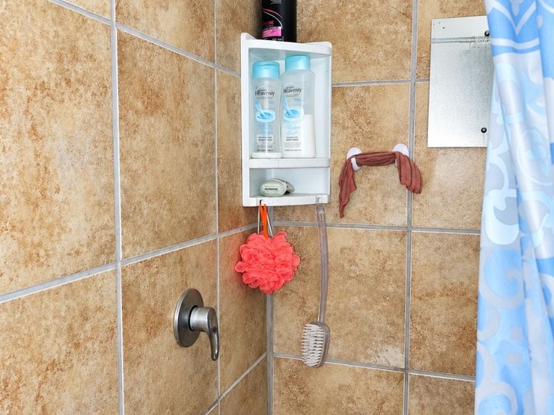 A functional shower enclosure featuring tan ceramic wall tiles, a standard shower head, and a built-in mixer tap.