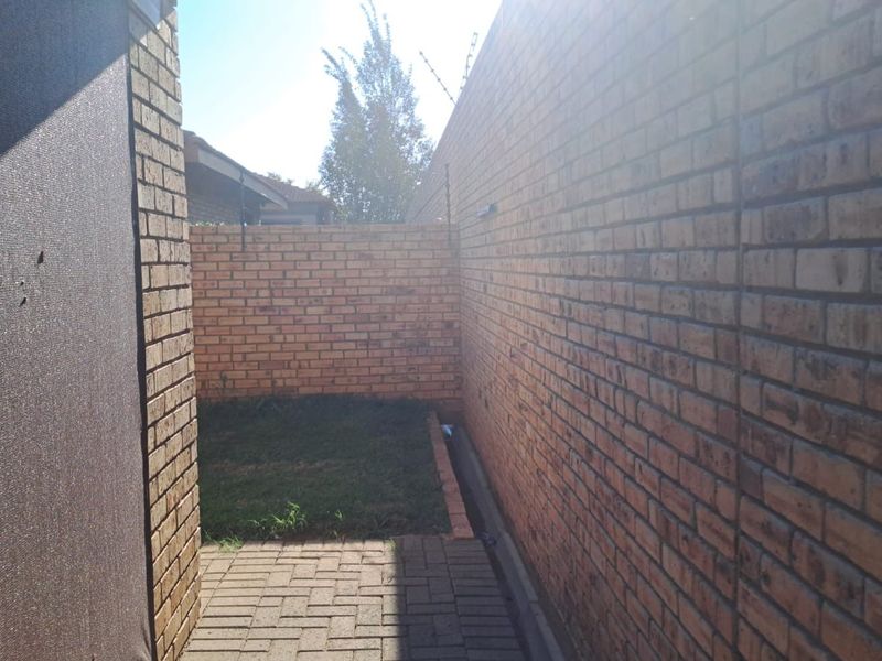 A narrow side or rear yard area featuring brick boundary walls, paved flooring, and electric security fencing.