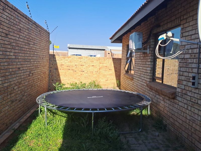 A side yard area featuring face brick walls, electric fencing, and an external air conditioning unit.