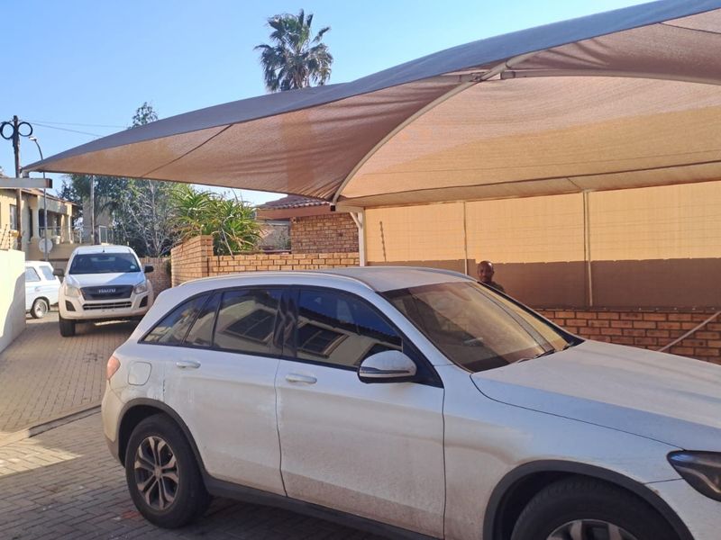 Front exterior view featuring a paved driveway, brick boundary wall with electric fencing, and a large shade sail for vehicle protection.