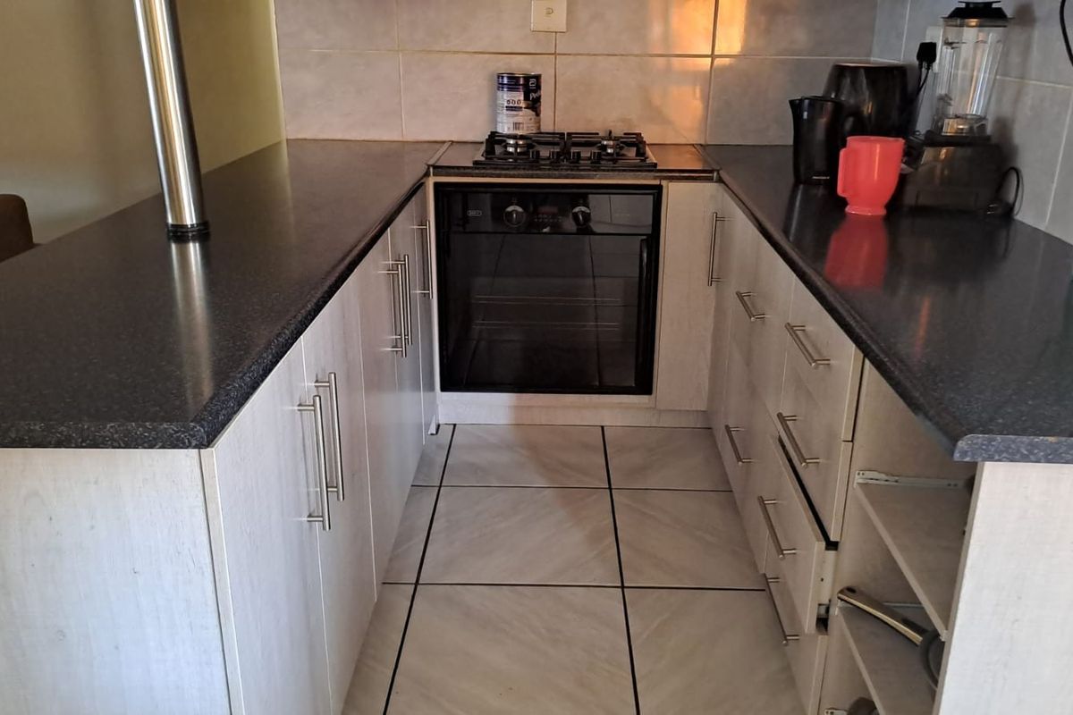 Compact kitchen featuring built-in oven, gas hob, laminate cabinetry, and tiled finishes. Note the missing drawer front on the lower cabinetry.